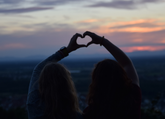 two friends making a heart with each of their hands outside at sunset