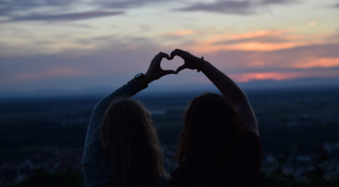 two friends making a heart with each of their hands outside at sunset