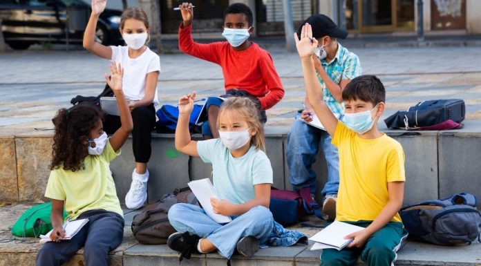 elementary-age kids wearing masks at school, raising hands to answer a question