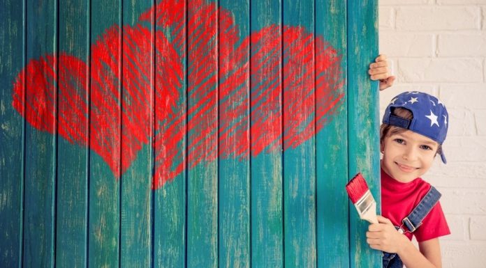 kid paints red hearts on turquoise wall