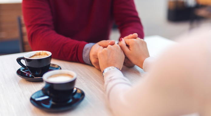 couple holding hands next to two cups of coffee