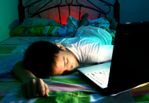 teen sleeping on bed next to open laptop