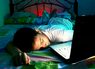teen sleeping on bed next to open laptop