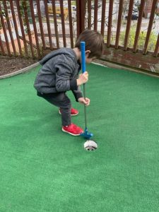 Toddler carefully putting golf ball into mini-golf hole at Parkville mini-golf
