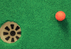 orange golf ball next to mini golf hole