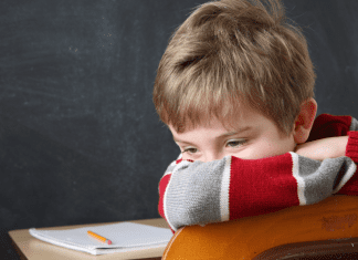 White male child sitting at desk with his face turned away from schoolwork.