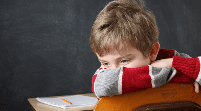 White male child sitting at desk with his face turned away from schoolwork.