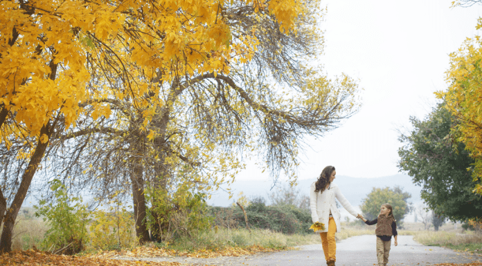 Woman and daughter walking outside amid yellow and orange fall foliage