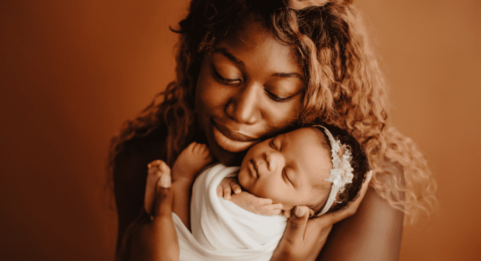Black mom holding new baby, both with eyes closed.