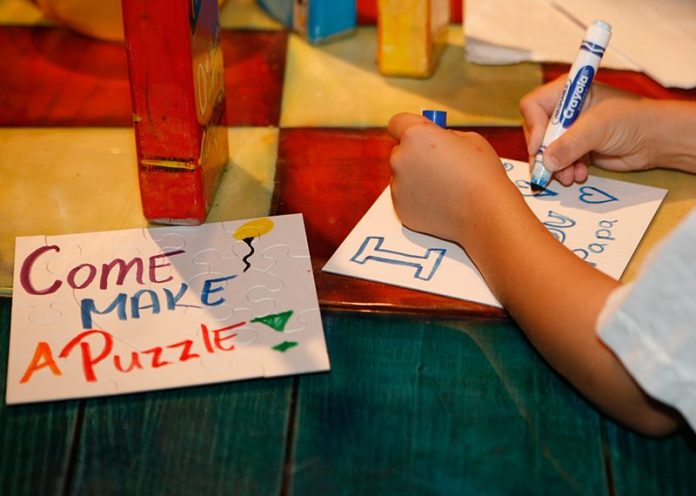 A child lettering a sign with a blue marker next to a sign that says 