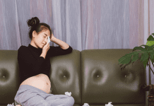 Pregnant Asian woman with top knot crying into facial tissue.