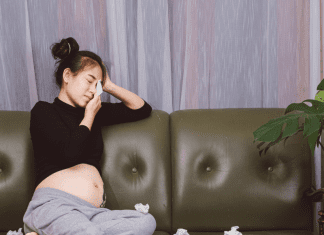 Pregnant Asian woman with top knot crying into facial tissue.