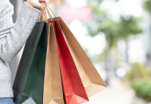 Tall mom shopping in gray sweater holding green, tan, red and another tan shopping bag,